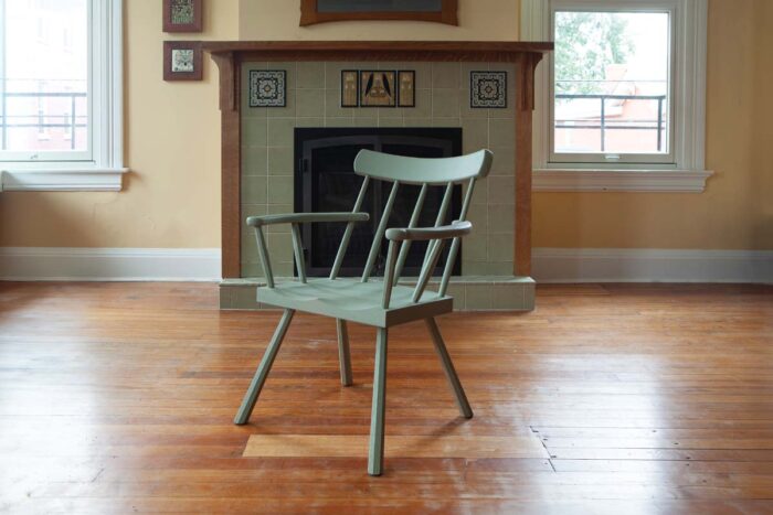 A painted chair sites in an empty room. The chair is painted a sage green. 